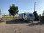 The exterior of the Elba's Rv and B and B RV Accommodation in Lethbridge Alberta. Pictured is an Rv set up on its plot of ground during bright and sunny day at the Rv BnB. beside the rv Campoer is a wooden picnic table and some trees for shade.