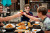 A group of men cheers their variously covered beers on the patio outside of the telegraph taphouse restaurant. Everyone in Frame is smiling while sitting at a table covered in local Lethbridge food.