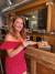 Sondra the Beer Maven Poses at a wooden bar with a dark malt beer in her hand and three other ones behind her. Sondra is wearing a red polka dot dress and red lipstick.