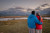 A couple in Waterton is looking off into the distance holding each other as they look at the moon sitting over a mountain range. the couple is wearing red and blue ajackets.